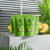 Green packages of Jackfruit with a sliced jackfruit on a white surface with plants in the background